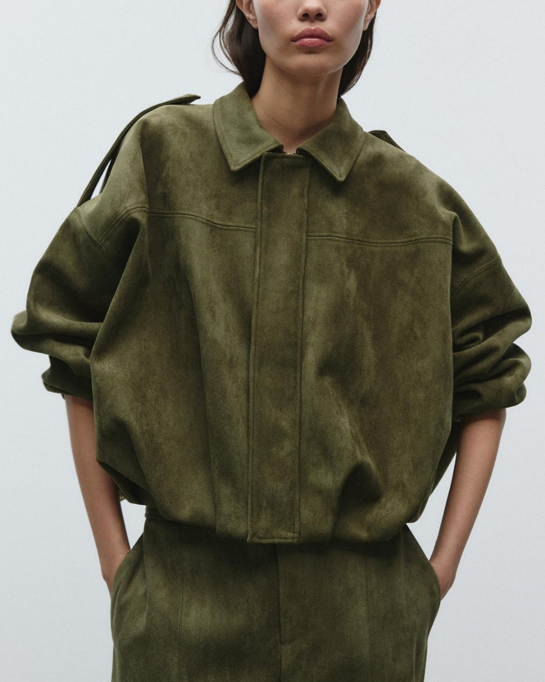 Person wearing a green suede jacket and pants on a plain background