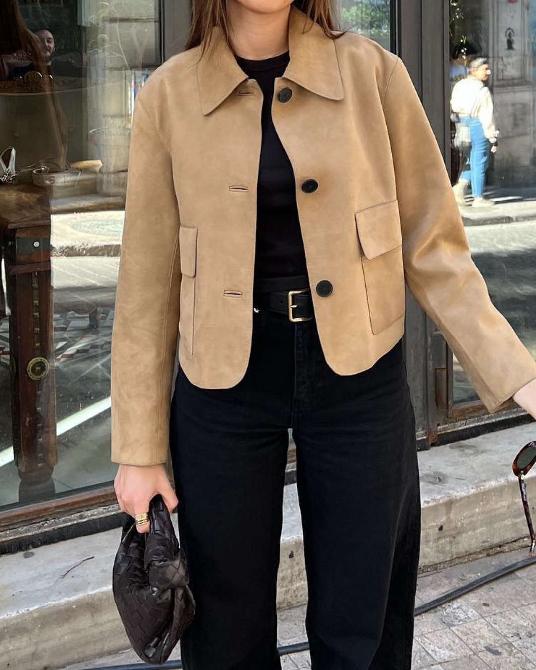 Person wearing a beige jacket and black pants on a city street.