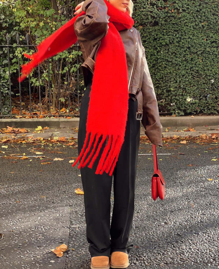 Person wearing a red scarf and holding a red handbag on a street with greenery in the background