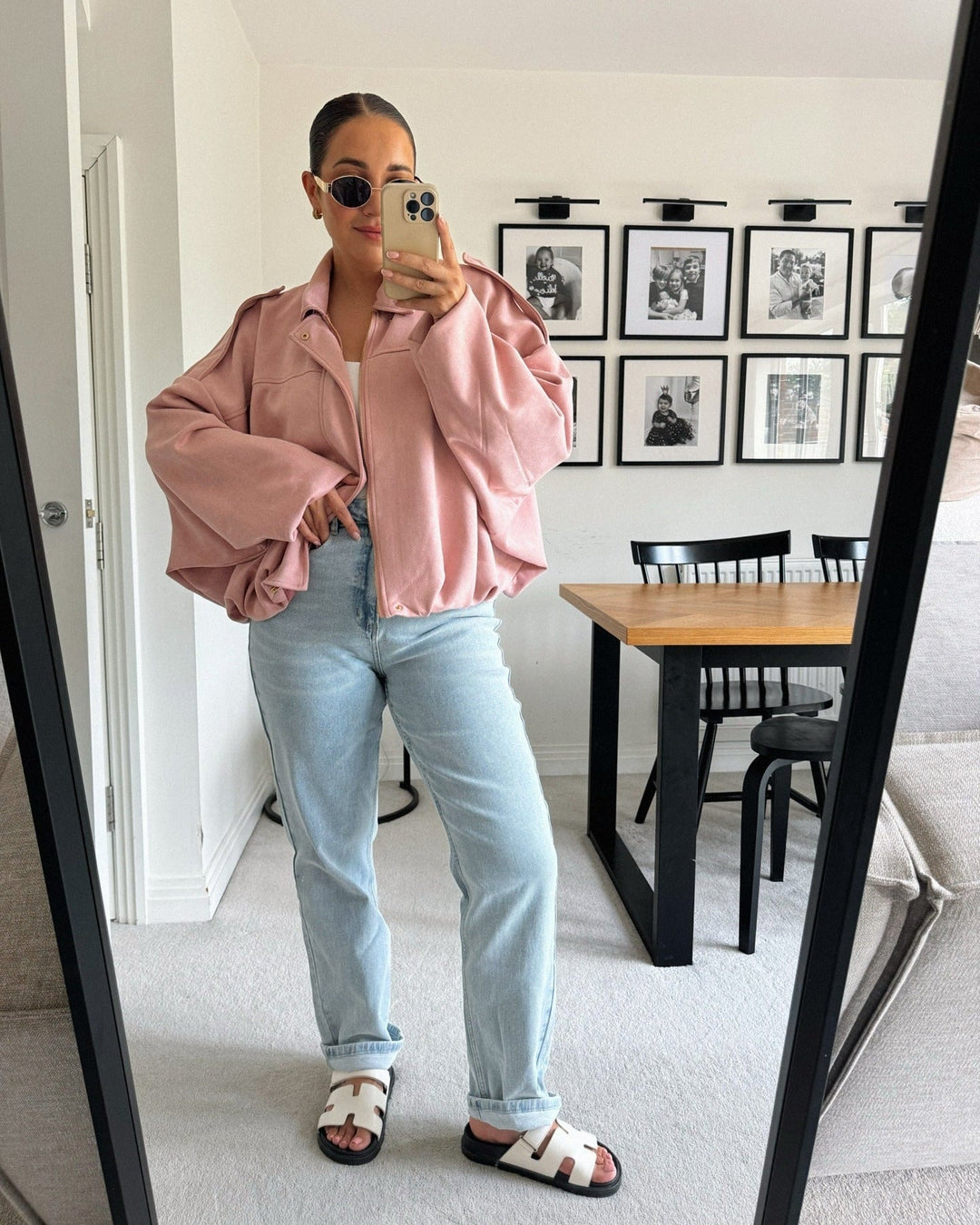 Person wearing a pink jacket and light blue jeans in a room with a dining table and chairs.