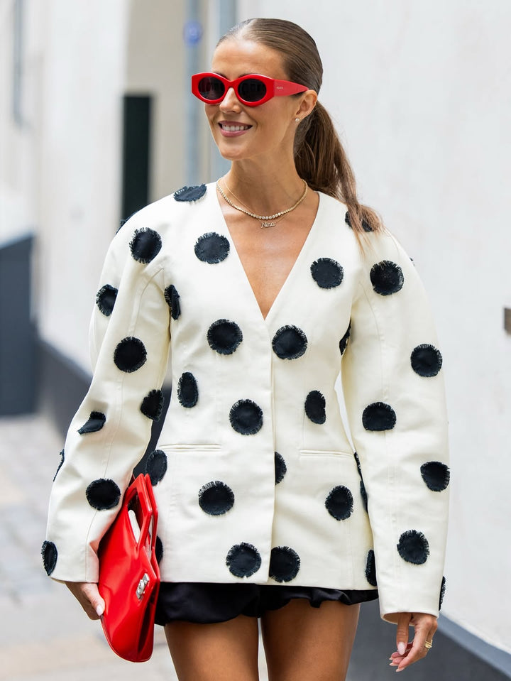 Woman wearing a polka dot cardigan and red sunglasses, holding a red clutch.