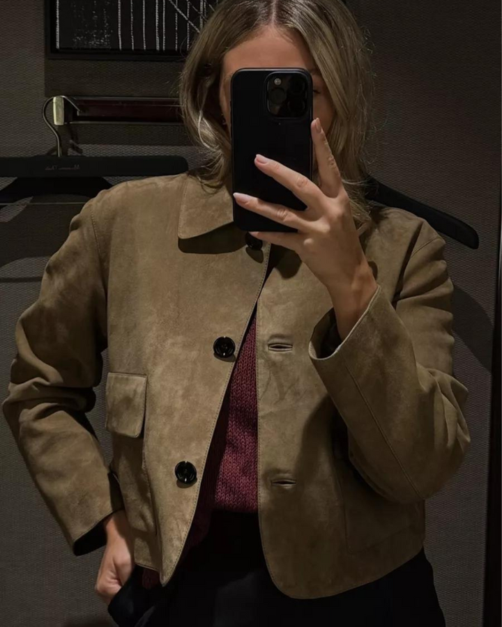 Person wearing a beige jacket taking a mirror selfie.