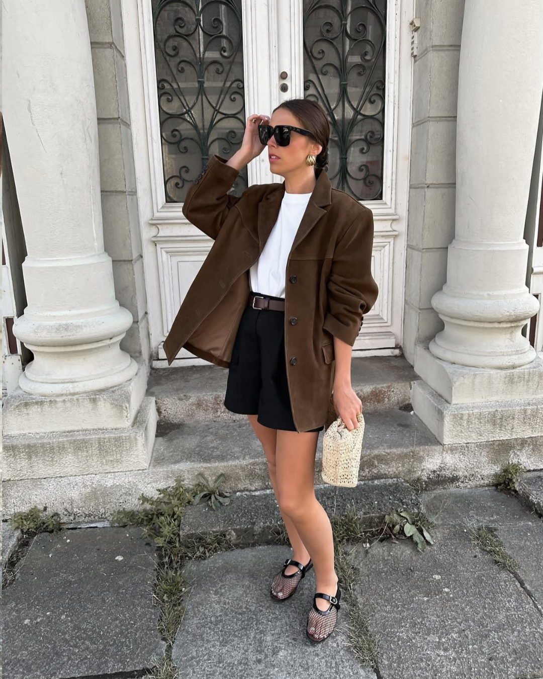 Woman in a brown blazer and black skirt standing on steps in front of a building.