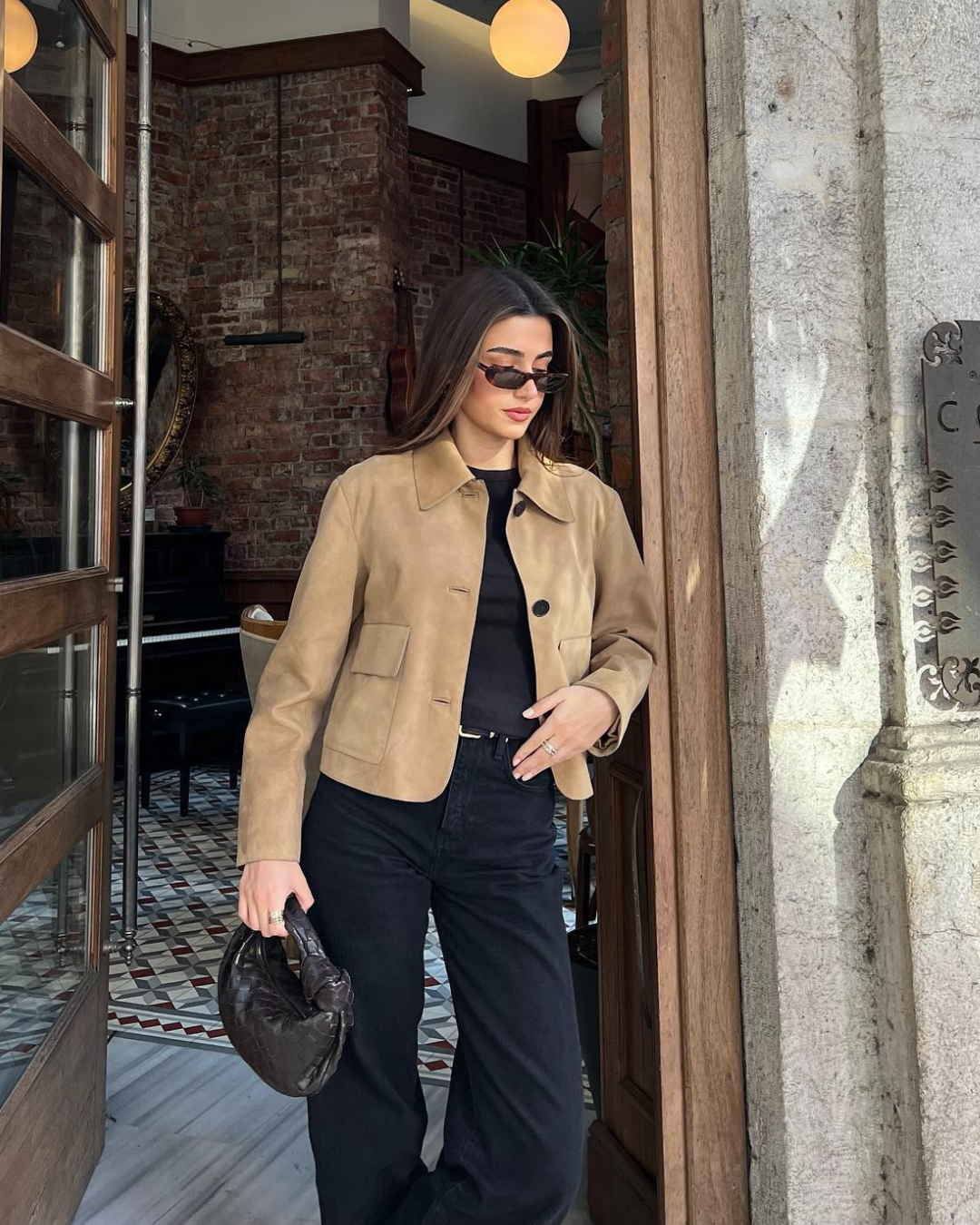 Woman in a beige jacket and black pants standing in a doorway.