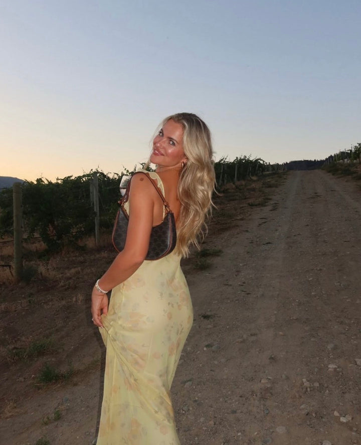 Woman in a yellow dress standing on a dirt road with vineyards in the background
