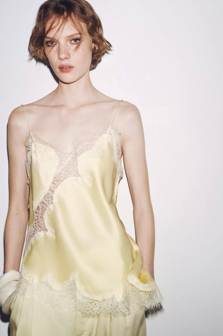 Woman wearing a light yellow slip dress with lace details on a plain background