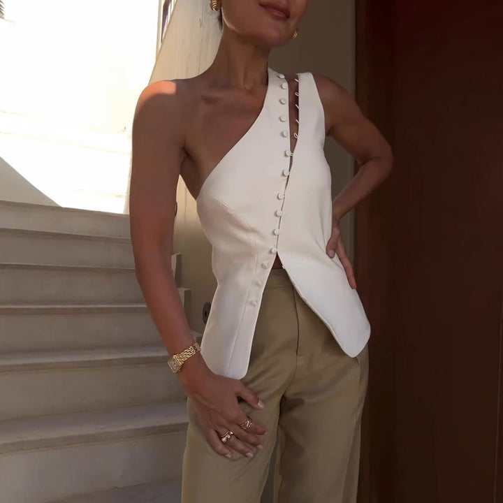 Woman wearing a white one-shoulder top and beige pants standing on a staircase.