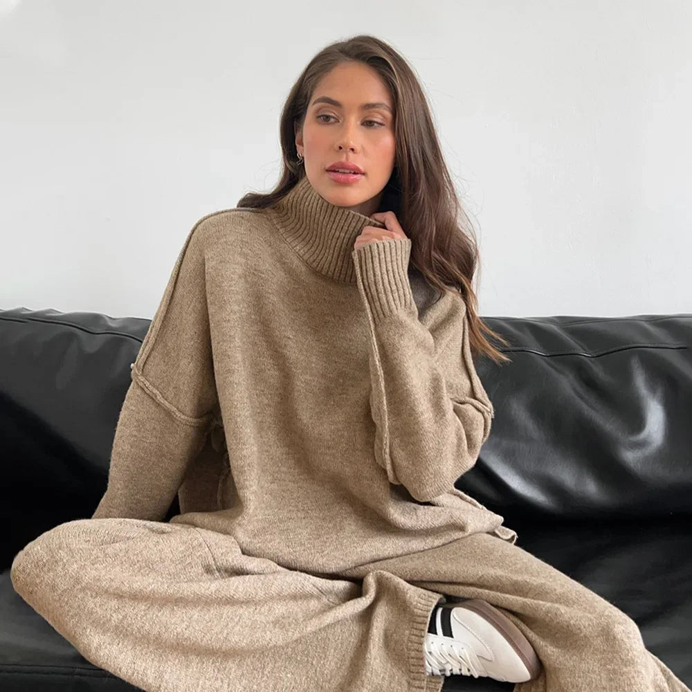 Woman wearing a beige sweater and pants sitting on a black leather couch.