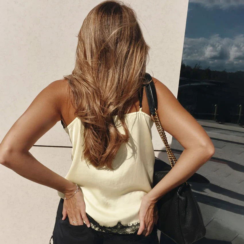 Woman in a light-colored top standing with hands on hips against a neutral wall.