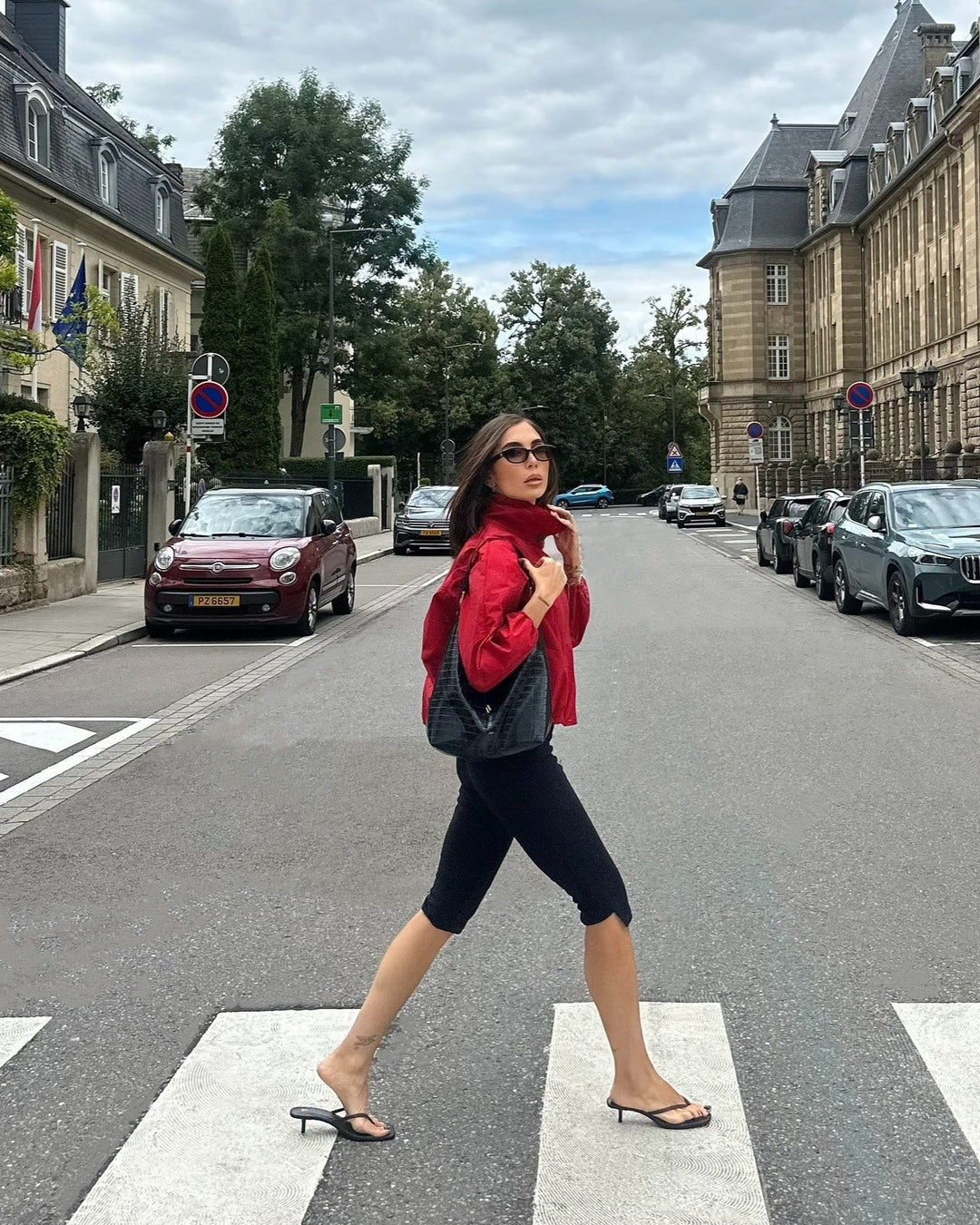 Woman in a red jacket crossing a street with buildings and cars in the background