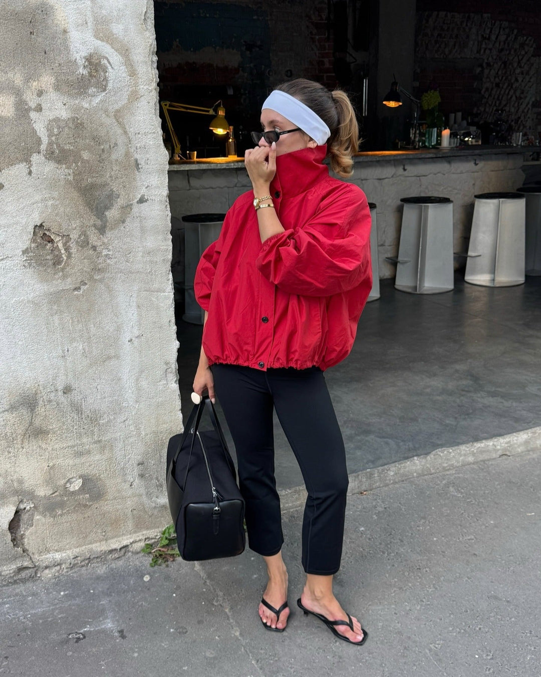 Person wearing a red jacket and black pants standing against a textured wall.