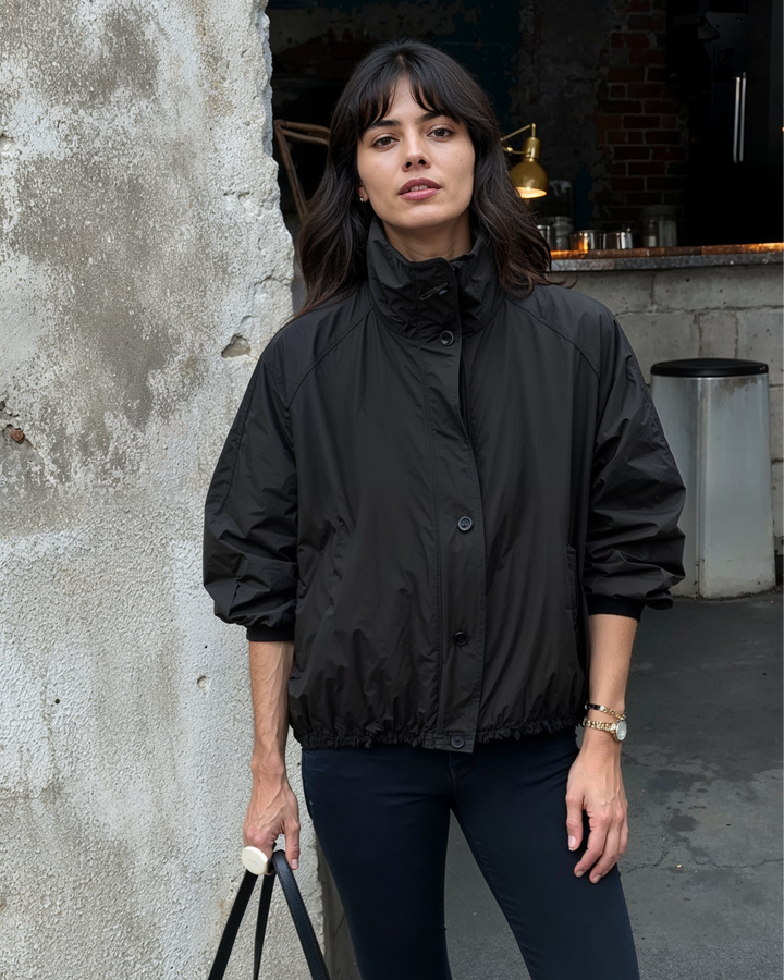 Woman wearing a black jacket standing against a textured wall.
